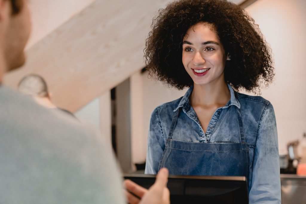 Confident helpful afro waitress servicing the customer at cash point in coffee shop