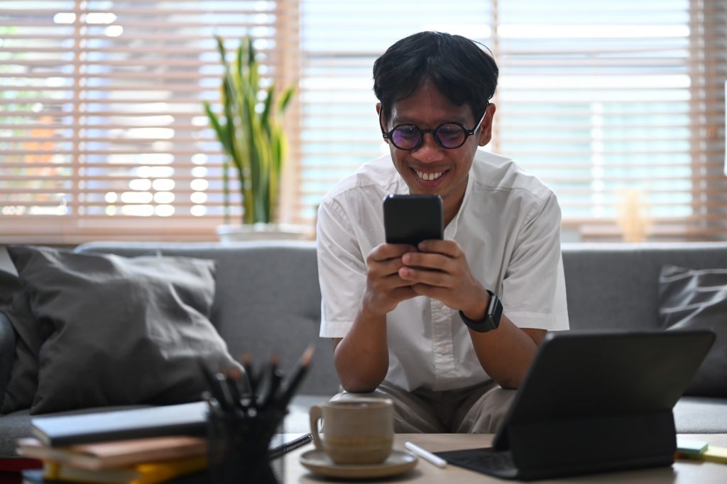 Smiling asian man checking social networking with smart phone at home.